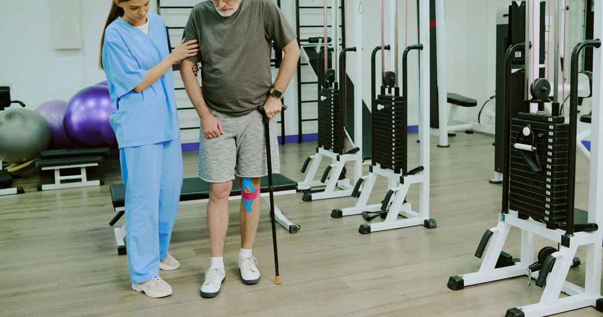 Bobath-Therapie als Hausbesuch in München – Physiotherapie Köpple Physiotherapeutin unterstützt einen älteren Patienten Schritt für Schritt beim Gehtraining